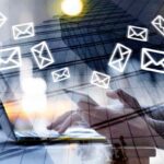 icone di lettere stilizzate con sullo sfondo mano che regge uno smartphone e altra che digita messaggio sulla tastiera del laptop