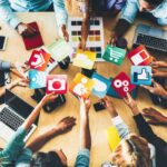 persone in cerchio con laptop e tablet con al centro icone di blog e social network