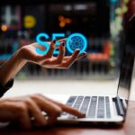 Scritta SEO in una mano davanti a un laptop